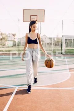 Beautiful young sporty girl playing with the ball on the basketball court out Stock Photos