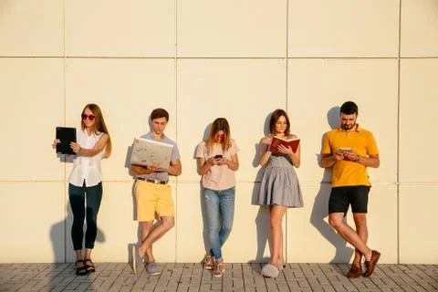 Beautiful young students are using gadgets, reading book and smiling, standin Stock Photos