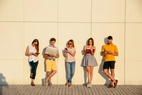 Beautiful young students are using gadgets, reading book and smiling, standin Stock Photos