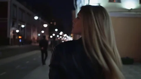 Beautiful young woman against night shined city. The blonde is walking around Stock Footage
