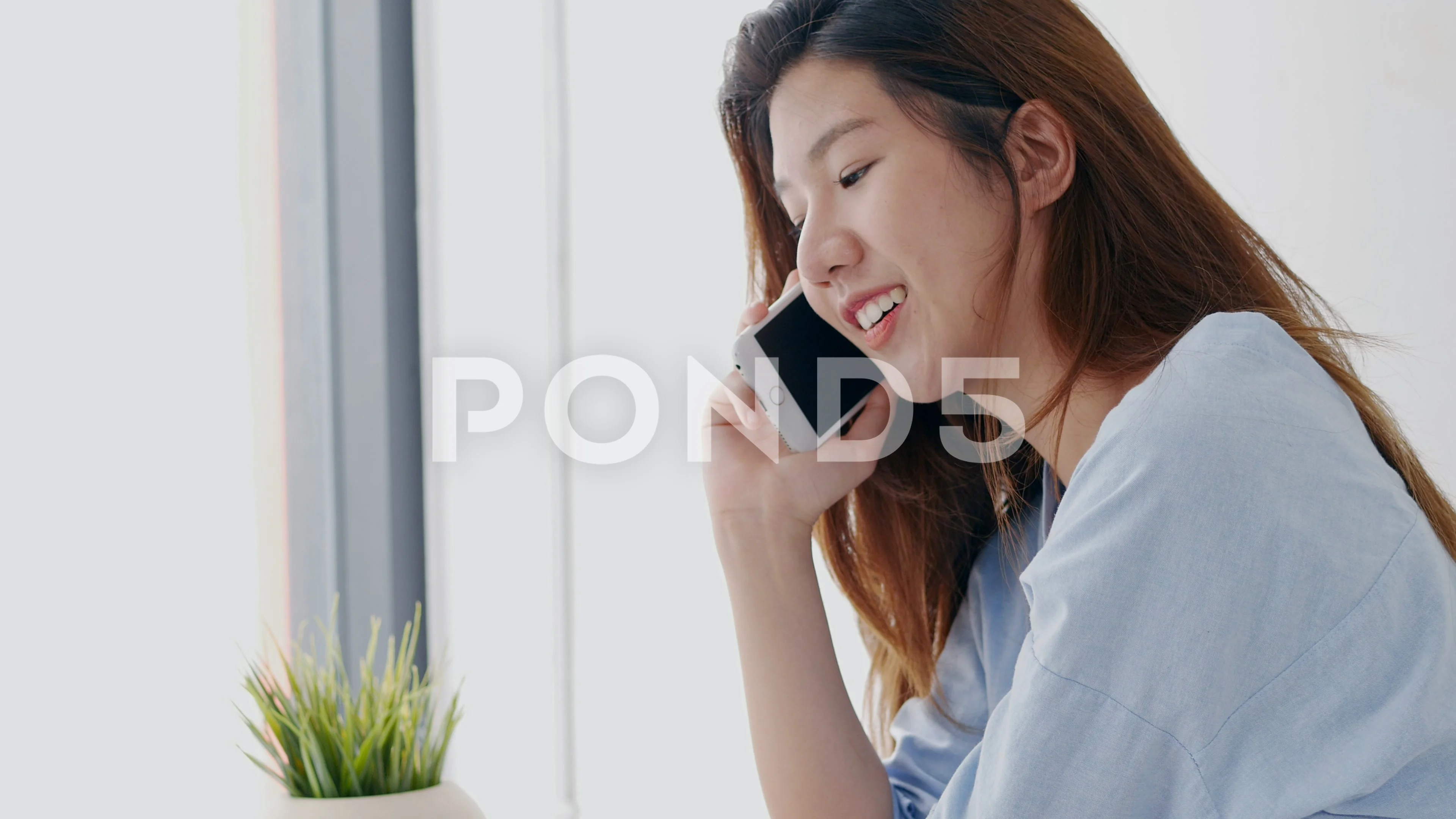 Beautiful young woman asian call phone beside the window in bedroom at home.