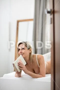 Beautiful young woman in bed, reading her favorite book (shallow DOF, color.. Stock Photos