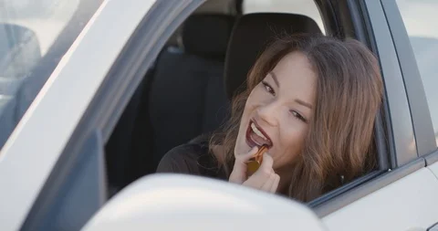 Beautiful young woman in the car using the mirror for tinting lips. Stock Footage