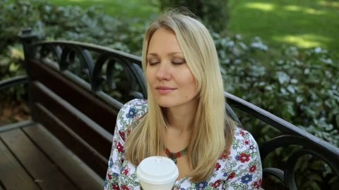 Beautiful young woman is drinking coffee on the bench. A girl is drinking tea Stock Footage