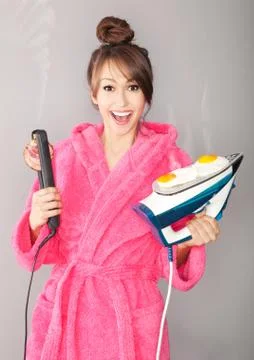 Beautiful young woman frying eggs and bacon on an iron and hair straightener Stock Photos