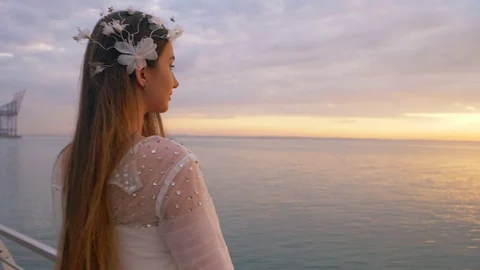 Beautiful young woman in long wedding dress standing near sea and looking on Stock Footage