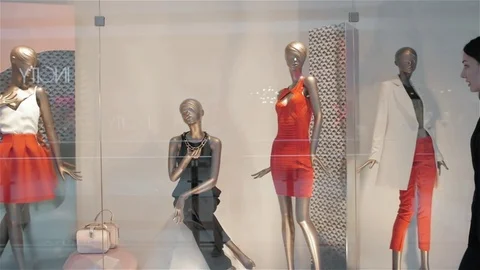 Beautiful young woman looking in a shop window with clothes and dresses and Stock Footage