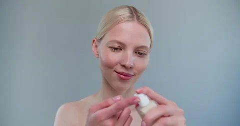 Beautiful young woman is missing while holding a facial cream standing isolated Video stock 153437147