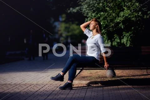 Beautiful young woman sits on a bench in the summer park Stock Photos