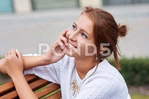 Beautiful young woman sits on a bench in the summer park Stock Photos