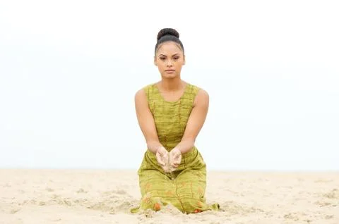Beautiful young woman sitting at the beach with sand flowing from hand Stock Photos