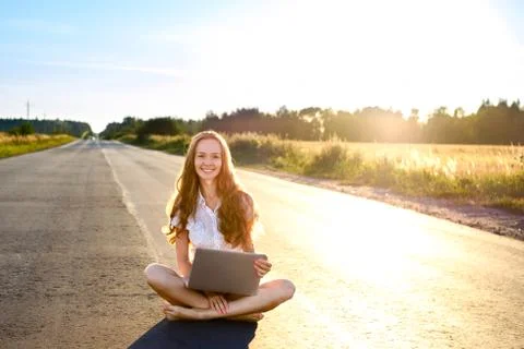 Beautiful young woman sitting with laptop and smiling on the road Stock Photos