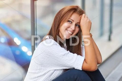 Beautiful young woman sitting near the glass building Stock Photos