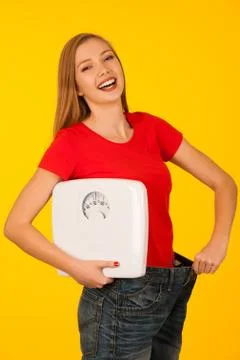 Beautiful young woman with too big trousers and scale gesture a weight loss o Stock Photos