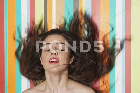 Beautiful young woman tossing hair against colorful striped background Stock Photos