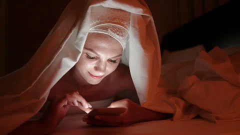 Beautiful young woman using smart phone under blanket in bedroom on bedtime Stock Footage 167940636