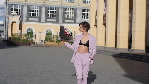 Beautiful young woman walks on a sidewalk near a city park, student girl holding Stock Footage