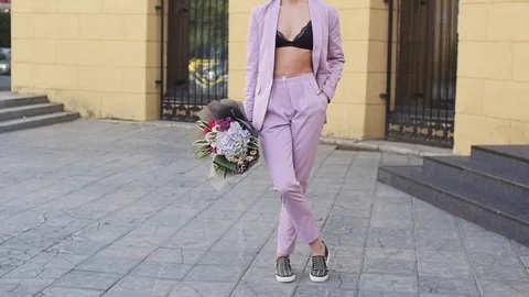 Beautiful young woman walks on a sidewalk near a city park, student girl holding Stock Footage