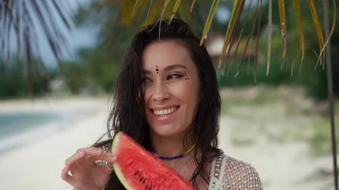 Beautiful young woman with watermelon on a tropical beach under a palm tree. Stock Footage