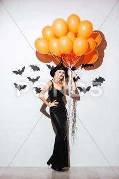 Beautiful young woman in witch halloween costume holding orange balloons Stock Photos