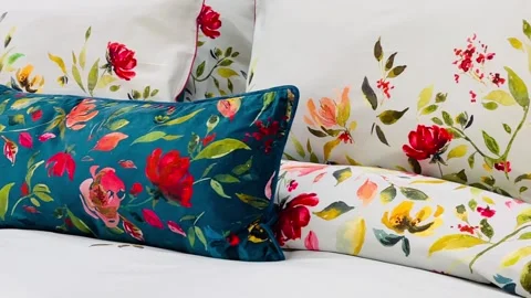 Beautifully arranged bed with floral-patterned pillows and white bedding. The Stock Footage 297085252
