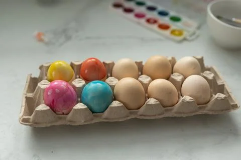 Beautifully Colorful Easter Eggs Displayed in a Carton Next to a Vibrant Wa.. Stock Photos