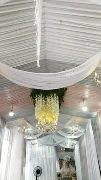 A beautifully decorated ceiling features white drapes and floral chandeliers  Stock Photos