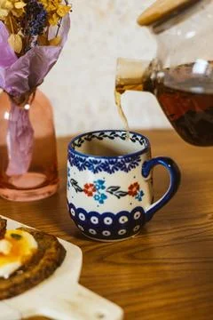 A beautifully patterned cup is filled with tea at a wooden table. Tea is being Stock Photos