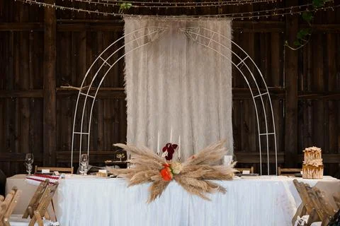 A beautifully styled wedding head table features a metal arch draped with she Stock Photos