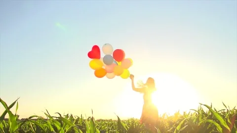 Beauty girl running on summer field with colorful balloons over clear blue sky Stock Footage