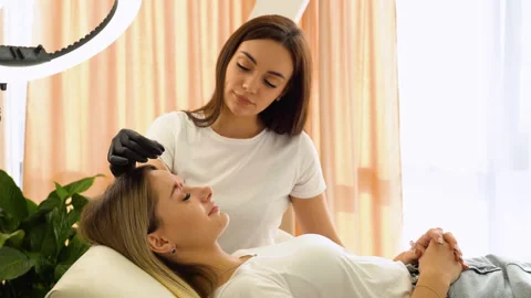 Beauty master brushing client's brows after permanent makeup procedure Stock Footage 255289048