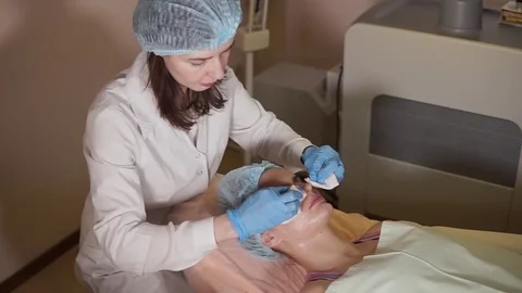 Beauty procedure. Beautician cleaning facial mask off from woman patient. Stock Footage