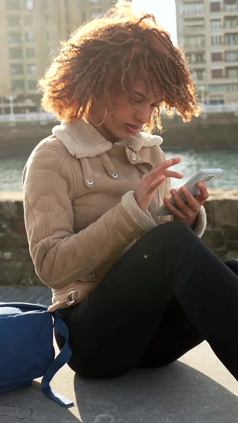 Beauty student using smartphone sitting on the city Stock Footage 295842572