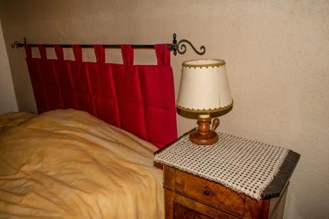 A bed and a bedside table with a rustic lamp in a country house. Stock Photos