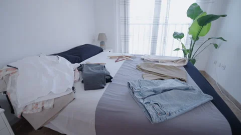 A bed in a bedroom with various items of clothing on it Stock Footage 257585774