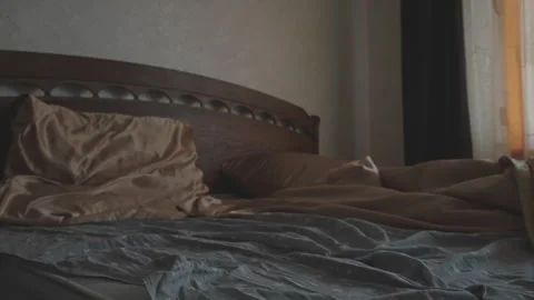 Bed with brown sheets and pillows in dimly lit room with muted colors and Video stock 268763542