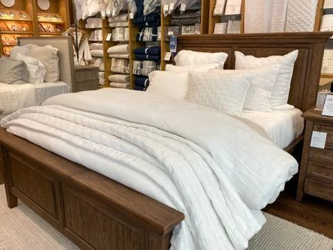 A bed with comforter, sheets, and pillows for sale at a  Pottery Barn at an i Stock Photos