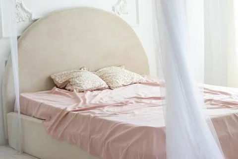 The bed is covered with a pink blanket and stands in a room flooded with white Stock Photos