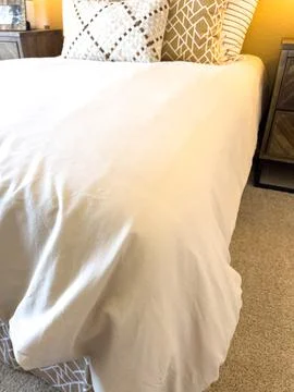 Bed Edge with White Comforter and Beige Carpet Foto stock