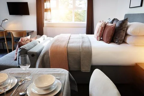 Bed, empty room and hotel accommodation or service dinner meal with interior Stock Photos