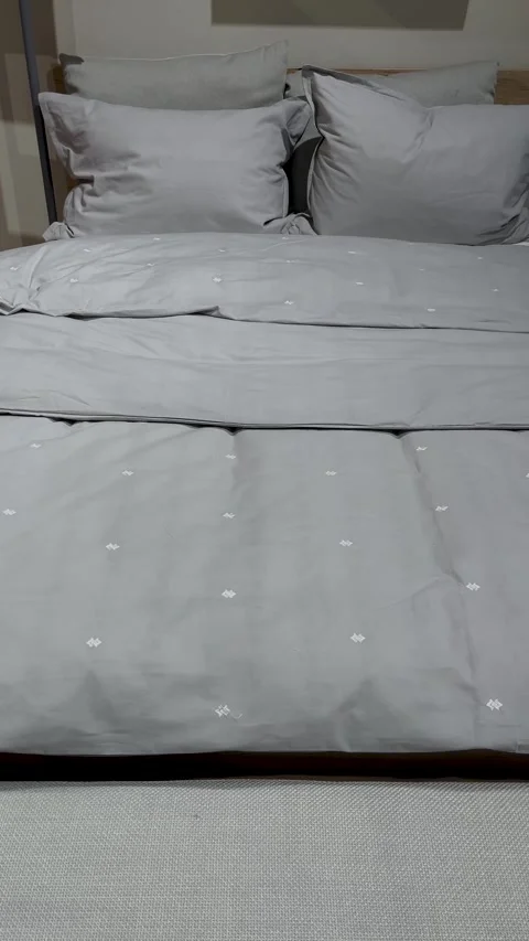 A bed with a gray bed - a blanket and pillows, next to a cabinet with a lamp. Stock Footage 316315964