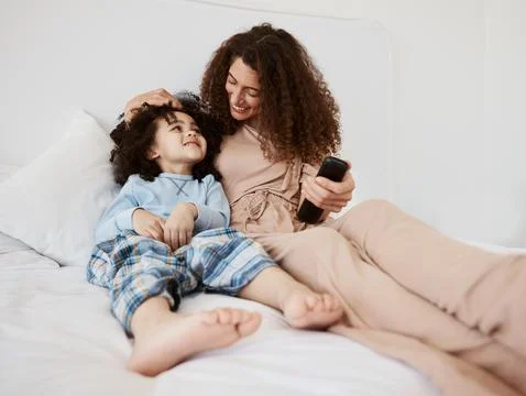 Bed, happy family child and mom watching tv series, movie and bonding with son Stock Photos