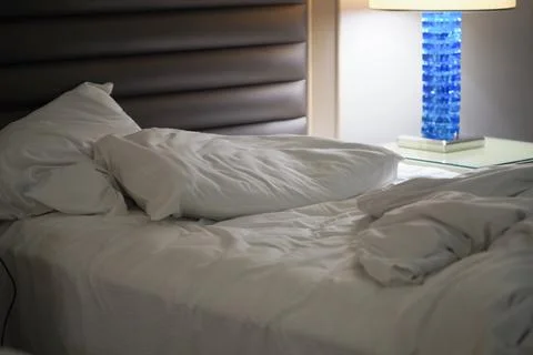 Bed with messy sheets and pillows in hotel room at night Stock Photos