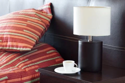Bed with a pillow, a cup of tea on the bedside table and lamp Stock Photos