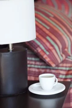 Bed with a pillow, a cup of tea on the bedside table and lamp Stock Photos