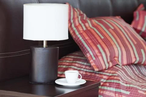 Bed with a pillow, a cup of tea on the bedside table and lamp Stock Photos