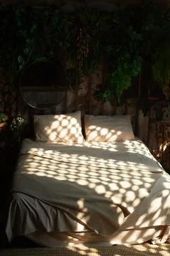 Bed with plain linen, with spots of light from the blinds. Cozy boho style Foto stock