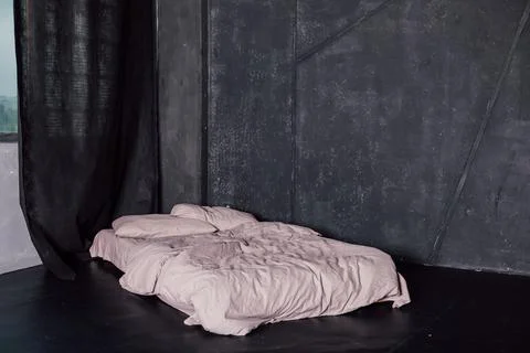 Bed with white bed standing in a dark room near the window Foto stock