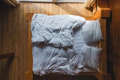 Bed with white bedding near the window in wooden house Stock Photos