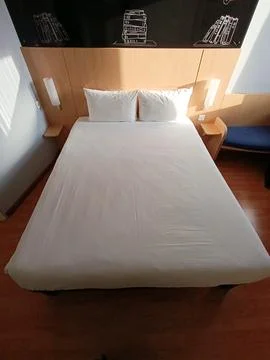 A bed with white sheets and pillows in a room Stock Photos